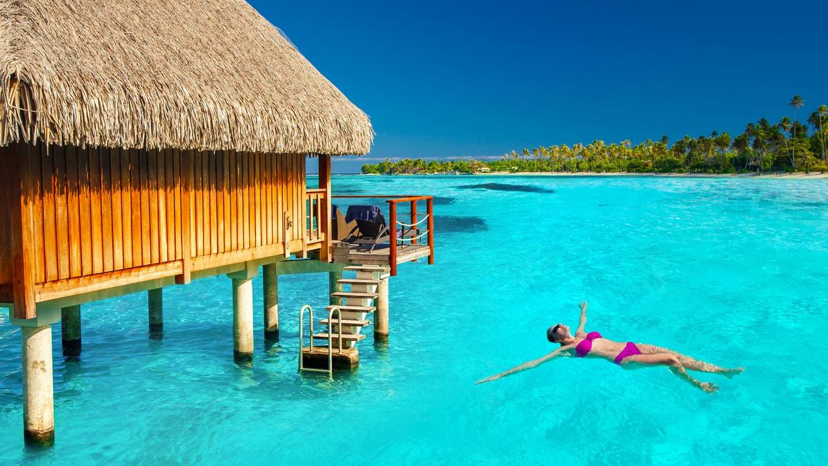 39174827 - woman swimming in tropical lagoon next to overwater villa