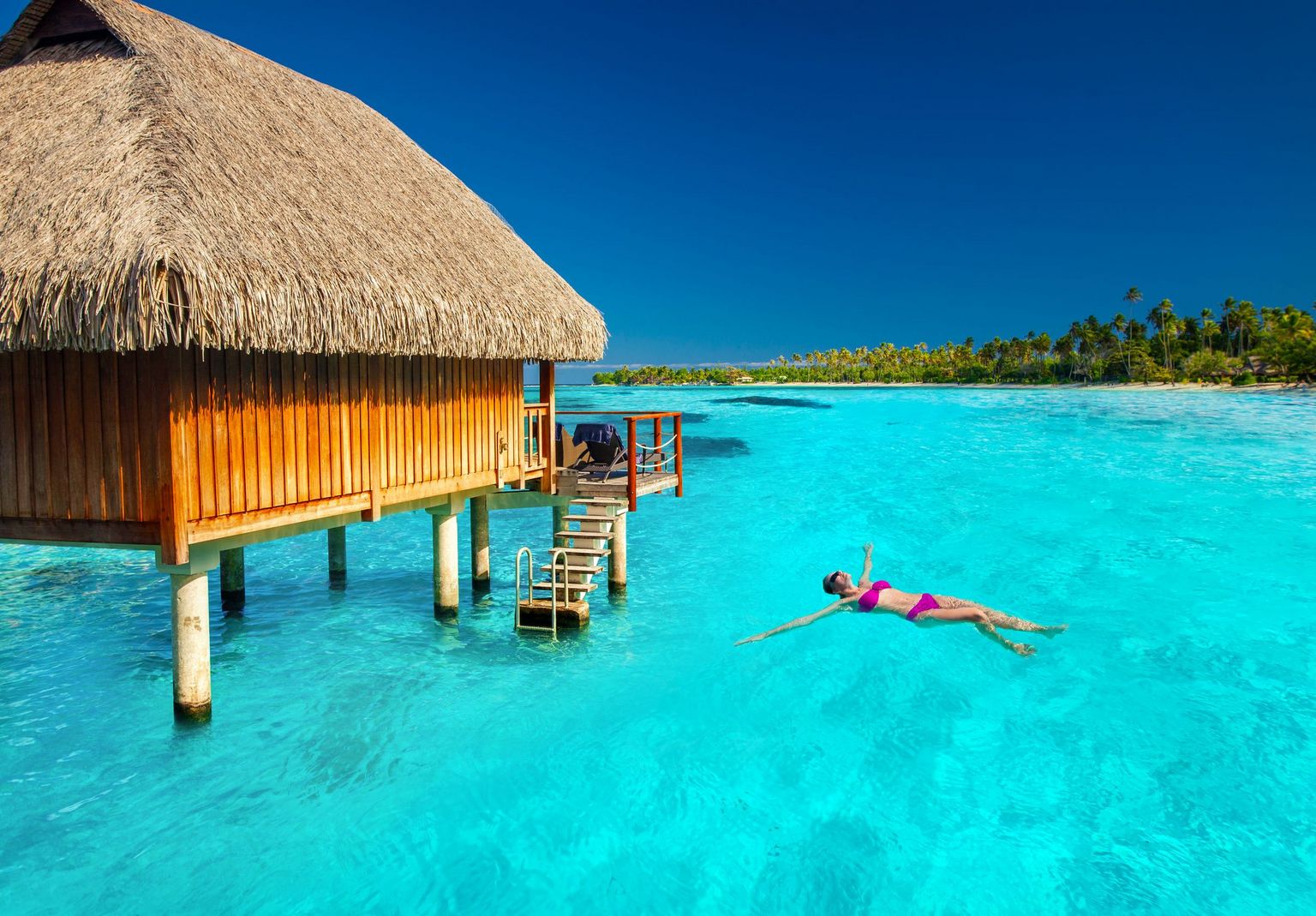 39174827 - woman swimming in tropical lagoon next to overwater villa